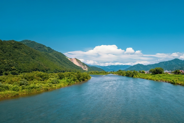 青空の下に広がる山々と清流の風景
