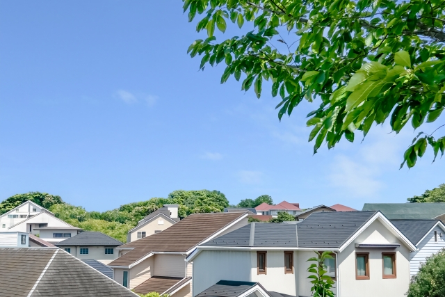 青空の下に広がる住宅街の屋根と緑の木々
