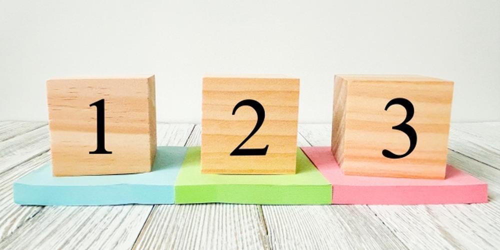 木目の床の上にカラフルな台座と木製ブロックが置かれ、それぞれに「1」「2」「3」と書かれたシンプルな数字のイメージ。画像は白背景に黒枠で囲まれている。