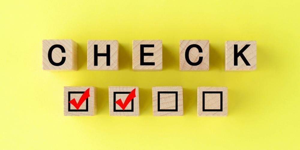 黄色い背景に並べられた木製ブロックに「CHECK」と黒文字で表示され、下には赤いチェックマークの付いたチェックボックスがある。画像は中央に配置され、黒い枠で囲まれている。