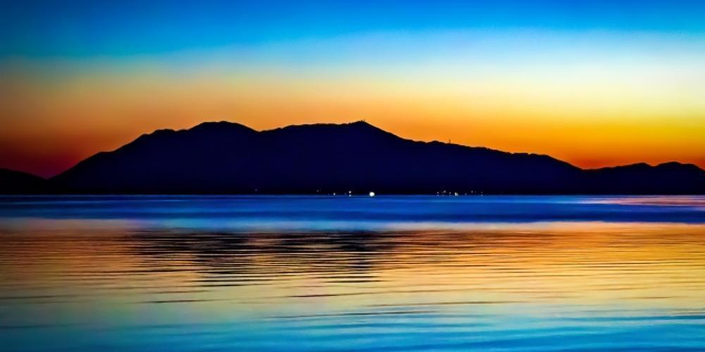 夕焼けに染まる湖とシルエットの山並み